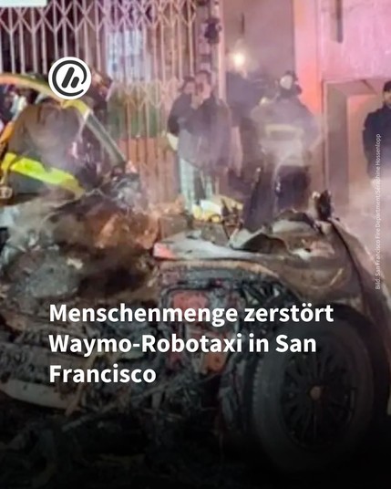 Bild: Im Hintergrund sieht man das zerstörte Robotertaxi von Waymo.

Überschrift: Menschenmenge zerstört Waymo-Robotaxi in San Francisco.